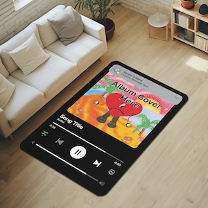 May include: Black and white music player rug with a colourful album cover featuring a cartoon heart with a sad face. The album cover text reads "Album Cover Here". The rug has a play button, pause button, and volume control.