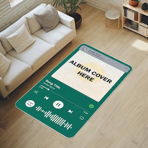 Pode incluir: Um tapete retangular verde projetado para se assemelhar a uma interface de reprodutor de música. O tapete apresenta o texto "ALBUM COVER HERE" e controles de música. O tapete está colocado em um piso de madeira perto de um sofá branco.