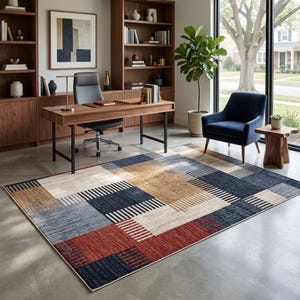 May include: A rectangular rug with a geometric pattern in red, blue, beige, and brown. The rug has a patchwork design with blocks of colour and striped accents. It is placed in a home office setting.