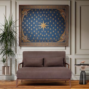 May include: A framed artwork with a blue background and gold stars hangs above a brown loveseat with two matching cushions. The artwork features a large gold star in the centre. A small side table and a potted plant are also in the room.