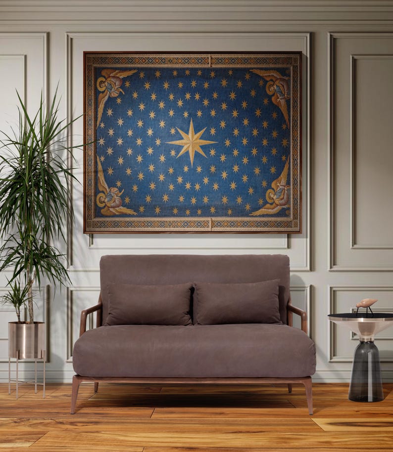 May include: A framed artwork with a blue background and gold stars hangs above a brown loveseat with two matching cushions. The artwork features a large gold star in the centre. A small side table and a potted plant are also in the room.