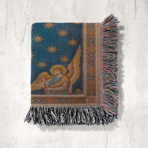 May include: A woven throw blanket with a celestial design. It has a blue background with gold stars and an angel with golden wings and a halo. The edges are trimmed with colourful fringe.