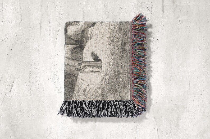 May include: A woven throw blanket with a black and white illustration of a figure in a room. The blanket has a fringe border with black, red, blue, and yellow threads. The blanket is displayed against a white textured wall.