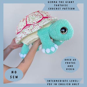 May include: A crochet tortoise plush toy with a mint green head and limbs, white feet, and a shell featuring a floral pattern with pink accents. Text reads: Gemma the Giant Tortoise Crochet Pattern, No Sew, Over 60 Photos and Video, Intermediate Level-PDF in English Only.