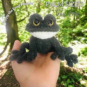 May include: A palm-sized, dark green crochet tree frog plushie with a white chest and large eyes with gold centers. The plushie is handmade and features the text "Poppy the Frog Plushie" and "Palm Sized Tree Frog".