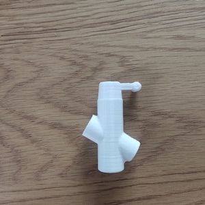 Op de afbeelding: Witte plastic drieweg-pijpfitting met een kleine knop bovenop.