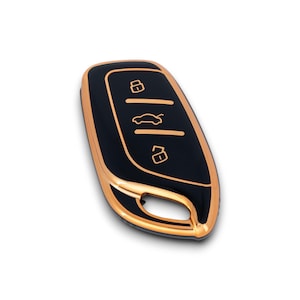 May include: Black car key with gold-colored trim. The key has three gold-colored icons: a lock, a car, and an unlocked lock. The key is on a white background.