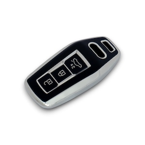 Pode incluir: Um chaveiro de carro preto e cromado com três botões e um ícone de carro. O chaveiro tem formato retangular com bordas arredondadas e uma borda cromada brilhante. Os botões incluem travar, destravar e abertura da mala.