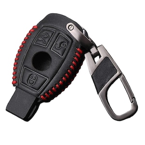 May include: Black leather key fob with red stitching and a silver metal key ring. The key fob has four buttons and a small hole for a key.