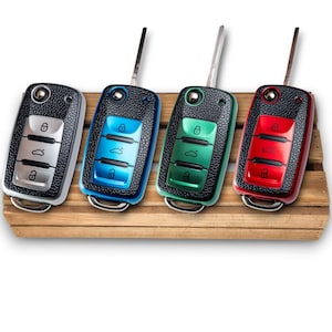 Può includere: Quattro telecomandi per auto in argento, blu, verde e rosso. Ogni telecomando ha un bordo nero con texture in pelle e una chiave in metallo. I pulsanti di ogni telecomando sono coordinati con il colore del bordo. I telecomandi sono esposti su una superficie di legno.