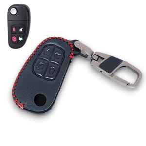 May include: Black leather car key fob cover with red stitching. The key fob has a silver metal clasp and a black leather accent. The key fob buttons are visible, and a separate key is shown to the left.