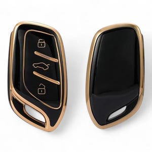 Puede incluir: Dos llaveros de coche con un diseño negro y dorado. Un llavero tiene botones para bloquear, desbloquear y abrir el maletero. El otro llavero es una pizarra en blanco.