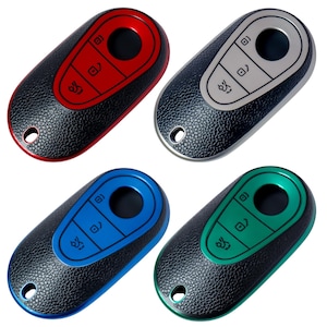 May include: Four car key fobs in red, silver, blue, and green. Each fob has a black textured body with a colored accent around the buttons. The buttons include lock, unlock, and trunk release symbols. A small hole is at the top for a key ring.