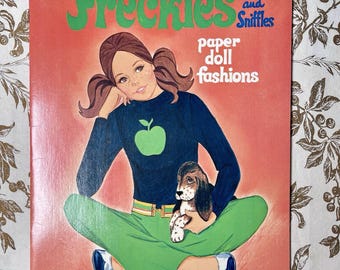 May include: Vintage Whitman's "Freckles and Sniffles" paper doll fashions book cover. The cover features a girl in a blue sweater with a green apple, green pants, and a puppy. The title is in green, with a red background.