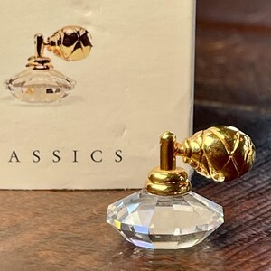 以下が含まれることがあります： ファセットクリスタルボディと金色の噴霧器を備えたミニチュア香水瓶。 ボトルは、丸くテクスチャ加工された上部を備えたクラシックなデザインです。「CLASSICS」という単語が背景に部分的に表示されています。