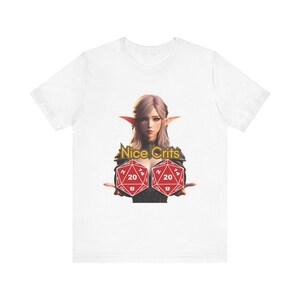 以下が含まれることがあります： 白いTシャツに、大きな赤い20面ダイスを2つ持った女性エルフのグラフィックがプリントされています。ダイスの上に「Nice Crits」というテキストがあります。