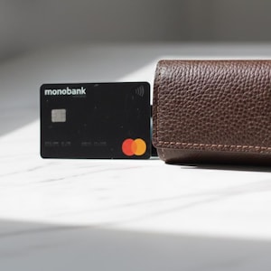 May include: A brown leather card holder with a textured surface sits next to a black credit card. The credit card has the word "monobank" printed on it, along with a Mastercard logo.