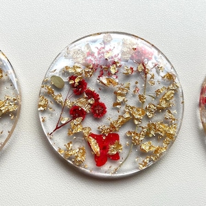 May include: Round clear resin coasters with red and gold pressed flowers and gold leaf accents.