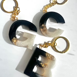 May include: Three resin letter keyrings with gold glitter and black and white ombre paint. The letters are G, C, and B.