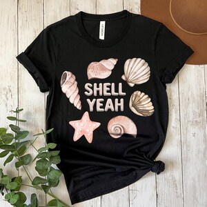 May include: Black t-shirt with a white graphic of seashells and the text "Shell Yeah".