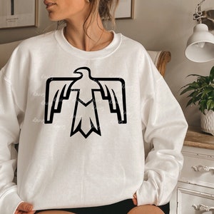 Puede incluir: Sudadera blanca con un diseño de águila estilizado en negro.