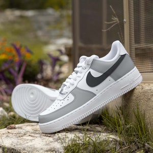 May include: White and gray low-top sneakers with a black swoosh logo and the word "AIR" on the side.