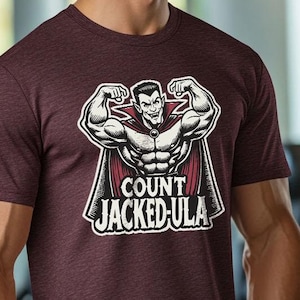 May include: Maroon crew neck t-shirt with a graphic of a muscular vampire flexing, with the text "COUNT JACKED-ULA". The image is in a gym setting. The shirt is made of a soft, comfortable material.