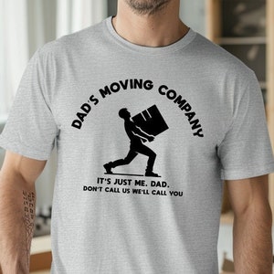 May include: A gray t-shirt with a black graphic of a person carrying a box. The text on the shirt reads "Dad's Moving Company. It's just me, Dad. Don't call us, we'll call you."