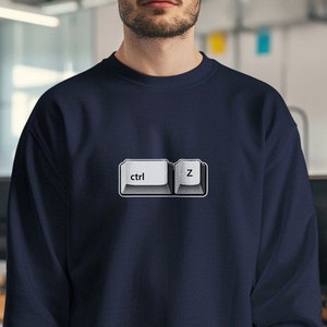 Puede incluir: Una sudadera azul marino con un gráfico blanco de las teclas 'ctrl' y 'z' de un teclado de computadora.