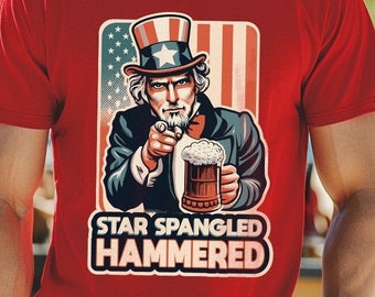 Puede incluir: Camiseta roja con una ilustración de dibujos animados del Tío Sam sosteniendo una jarra de cerveza y apuntando al espectador. El texto "Star Spangled Hammered" está impreso debajo de la ilustración.