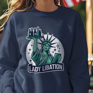 May include: A navy blue sweatshirt with a graphic of the Statue of Liberty holding a tray of beer bottles. The graphic is surrounded by stars and the text "Lady Libation".