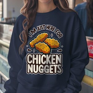 Puede incluir: Una sudadera azul marino con el texto "I'm just here for chicken nuggets" en blanco y un gráfico de nuggets de pollo.
