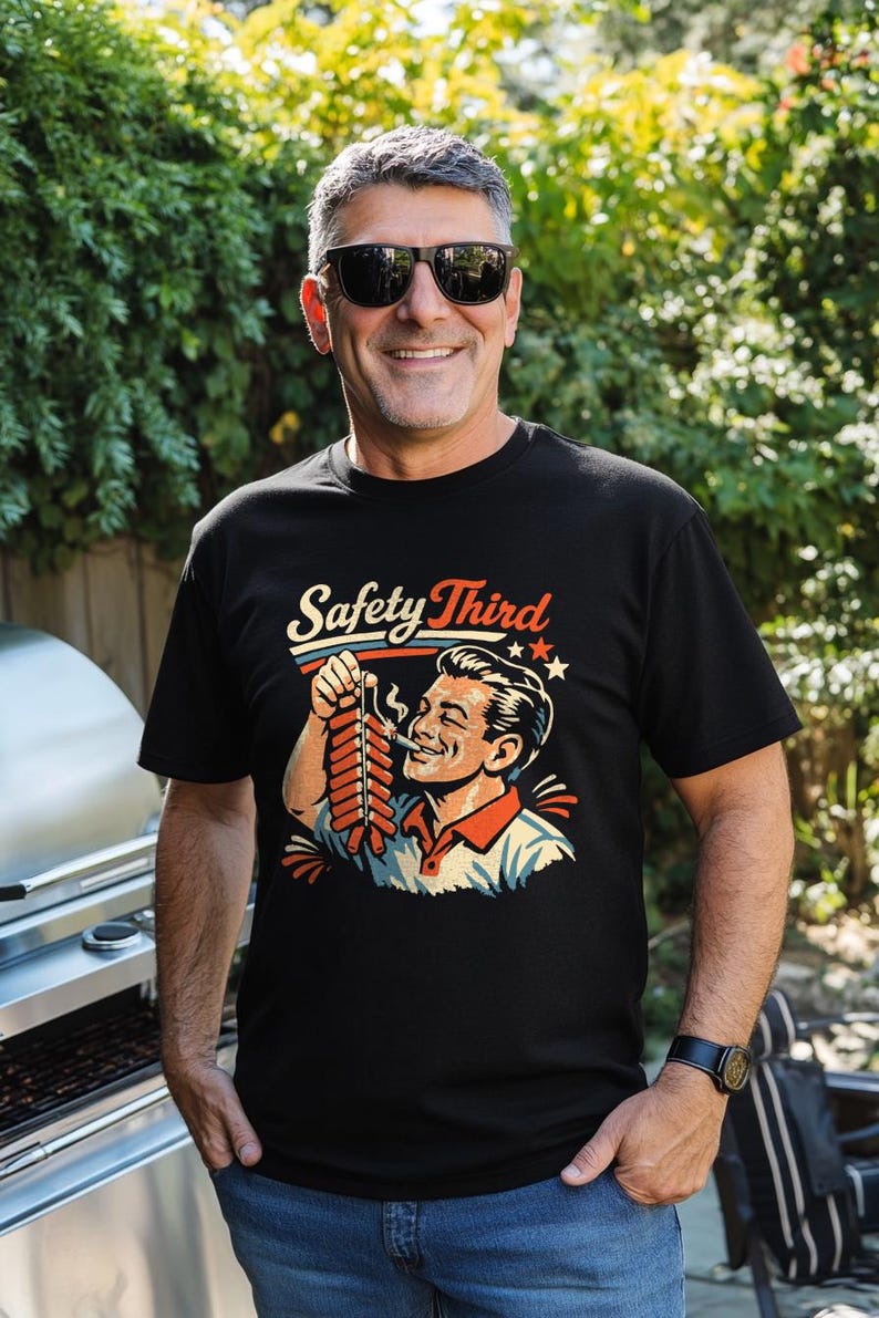 May include: Black t-shirt with the text "Safety Third" above a vintage illustration of a man smoking a firecracker. The graphic is in red, white, and blue. The man is wearing sunglasses and smiling.