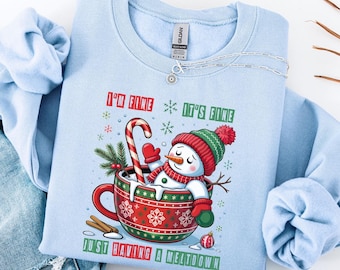 May include: Light blue sweatshirt with a snowman graphic inside a red and green cup, a candy cane, and the text "I'M FINE IT'S FINE JUST HAVING A MELTDOWN". The snowman wears a red and green hat and scarf.