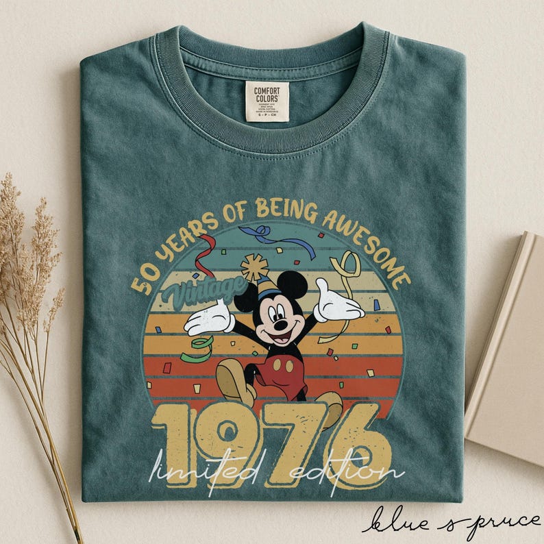 May include: Blue spruce t-shirt with a vintage Mickey Mouse design. The graphic includes the text "50 Years of Being Awesome" and "1976 Limited Edition". The design has a retro colour scheme with Mickey Mouse in a party hat.