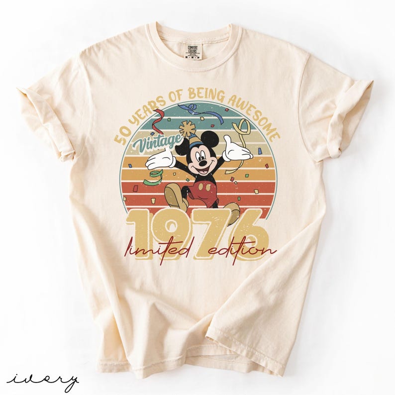 May include: Ivory t-shirt with a vintage Mickey Mouse design celebrating 50 years. The graphic includes the text "50 Years of Being Awesome," "Vintage," and "1976 Limited Edition" in a retro style, with a circular background.