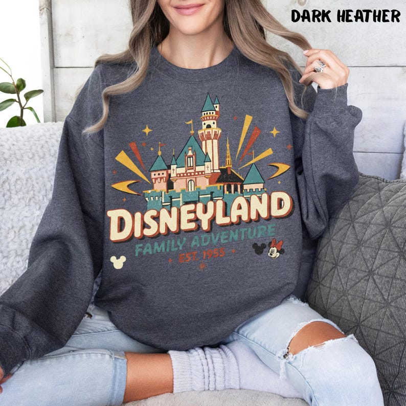 Puede incluir: Sudadera gris oscuro con un dise&ntilde;o de Disneyland. El dise&ntilde;o presenta un castillo, las palabras "Disneyland Family Adventure" y la fecha de fundaci&oacute;n de 1955. Mickey y Minnie Mouse tambi&eacute;n est&aacute;n presentes.
