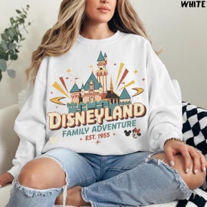 Puede incluir: Sudadera blanca con un gr&aacute;fico del castillo de Disneyland y el texto "Disneyland Family Adventure + Est. 1955". El dise&ntilde;o incluye acentos coloridos y siluetas de Mickey y Minnie Mouse. Una prenda superior casual y c&oacute;moda.