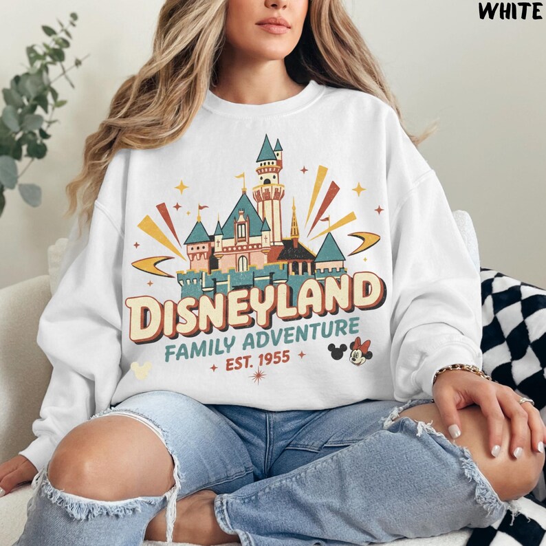 Puede incluir: Sudadera blanca con un gr&aacute;fico del castillo de Disneyland y el texto "Disneyland Family Adventure + Est. 1955". El dise&ntilde;o incluye acentos coloridos y siluetas de Mickey y Minnie Mouse. Una prenda superior casual y c&oacute;moda.