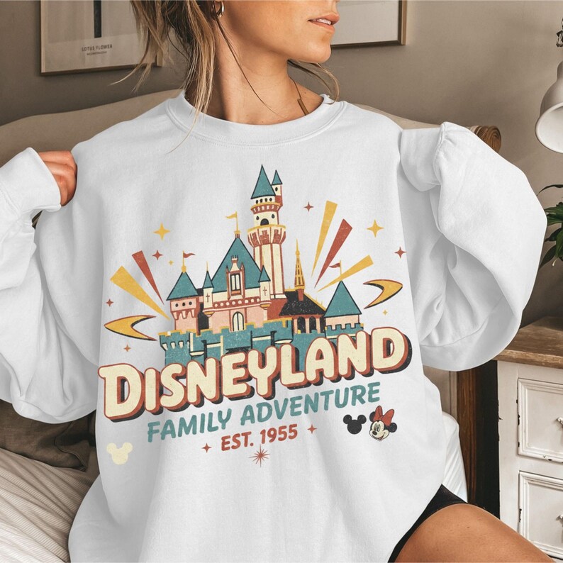 Puede incluir: Sudadera blanca con un gr&aacute;fico de Disneyland. El dise&ntilde;o incluye un castillo, la palabra "Disneyland" y la frase "Family Adventure Est. 1955". Mickey Mouse y estrellas tambi&eacute;n est&aacute;n incluidas en el dise&ntilde;o.