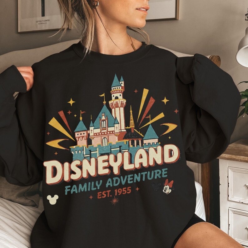 Puede incluir: Sudadera negra con un dise&ntilde;o de Disneyland. El dise&ntilde;o incluye un castillo, estrellas y las palabras "Disneyland Family Adventure Est. 1955" en un estilo vintage. Tambi&eacute;n hay un icono de Mickey Mouse.