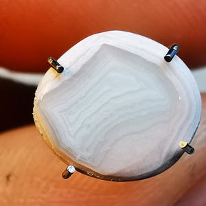 以下が含まれることがあります： 渦巻き模様の白いアゲートのカボション。4本の金属製の爪で固定されています。