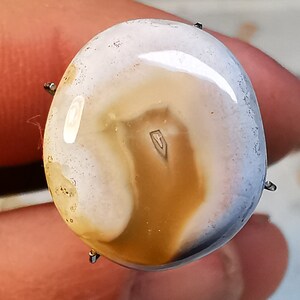 以下が含まれることがあります： 白と茶色のアゲートのcabochonで、表面は滑らかで磨かれています。石には渦巻きと線のユニークなパターンがあります。