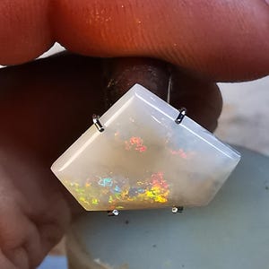 May include: A white opal gemstone with iridescent rainbow flashes, set in a silver prong setting.