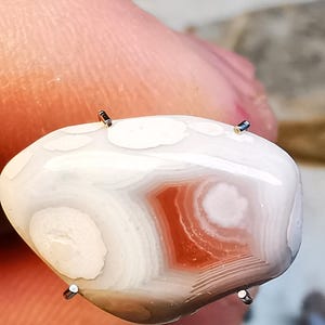 以下が含まれることがあります： 赤とピンクの縞模様のある白い瑪瑙の石。石は磨かれており、表面は滑らかです。