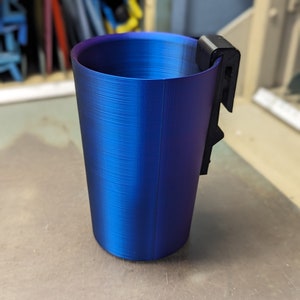 May include: A blue and purple plastic cup with a black clip on the side. The cup has a textured surface.