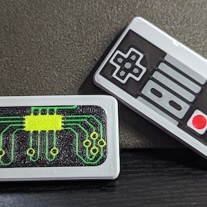 May include: Two white plastic keychains, one with a black and green circuit board design and the other with a black and white Nintendo controller design.