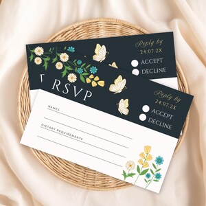 Op de afbeelding: Twee zwarte RSVP-kaarten met witte tekst en bloemmotieven. De kaarten hebben een sectie voor namen, dieetwensen en een antwoorddatum van 24.07.2X. De kaarten hebben ook een sectie om de uitnodiging te accepteren of te weigeren.