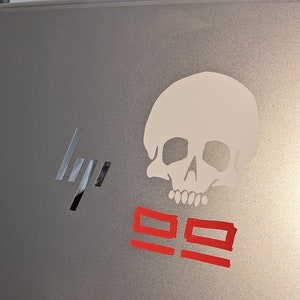 May include: A silver laptop with a white skull sticker and red "99" markings.