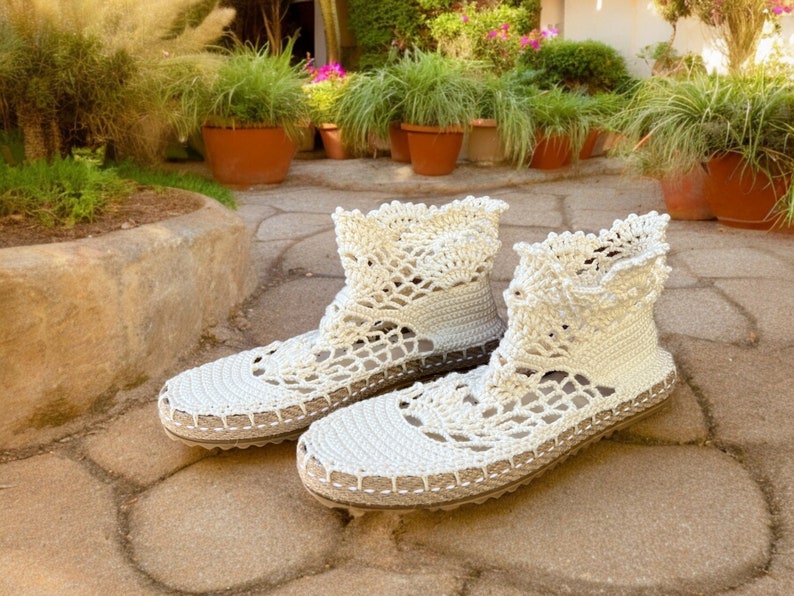 May include: A pair of white crocheted ankle boots with a delicate lace pattern. The boots have a flat sole and are made of a soft, lightweight material.